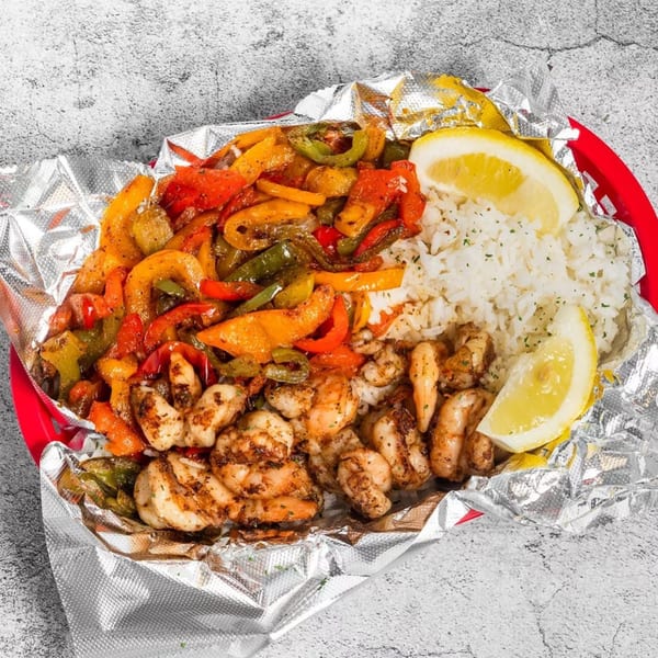Grilled shrimp with colorful bell peppers, white rice, and lemon wedges in a foil-lined basket.