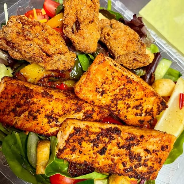 A seafood salad with three pieces of blackened salmon and four pieces of fried fish over greens.